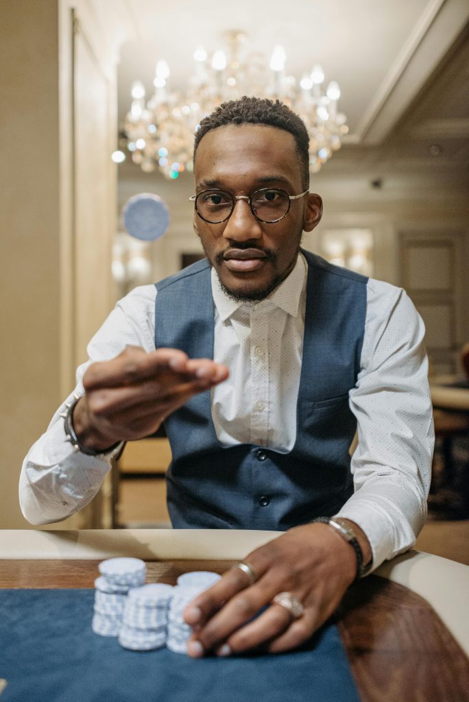 A focused African American man in a casino betting with poker chips, a chandelier in the background.